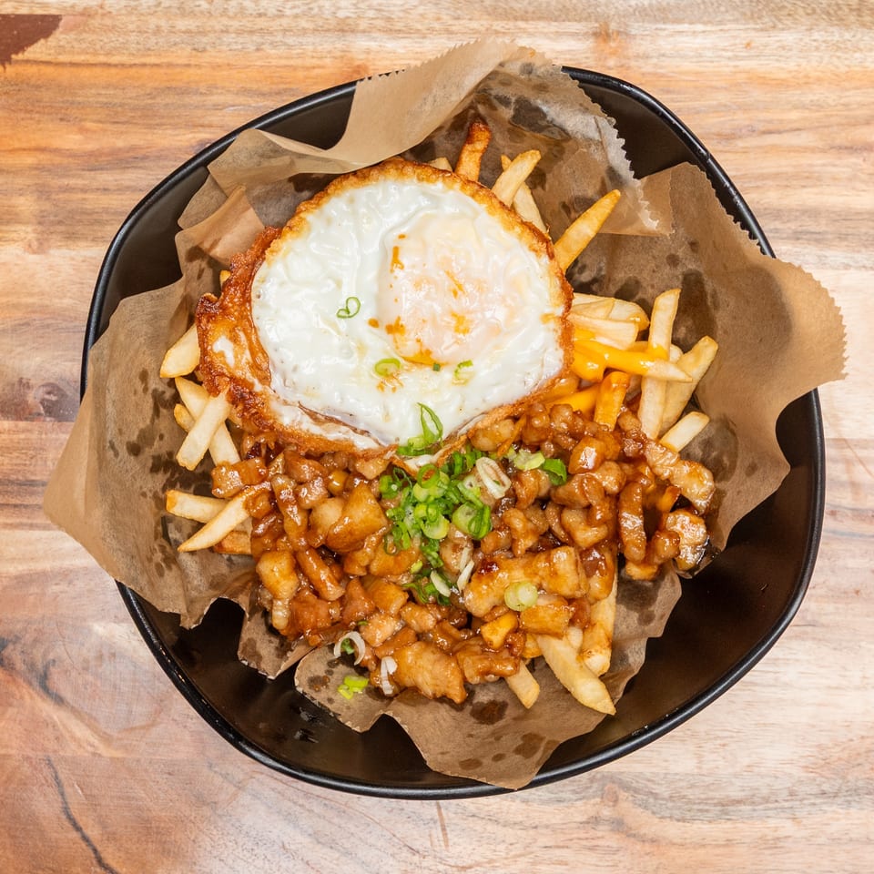 Loaded fries topped with crispy chicken, brown sauce, a fried egg, and sliced green onions in a black bowl.