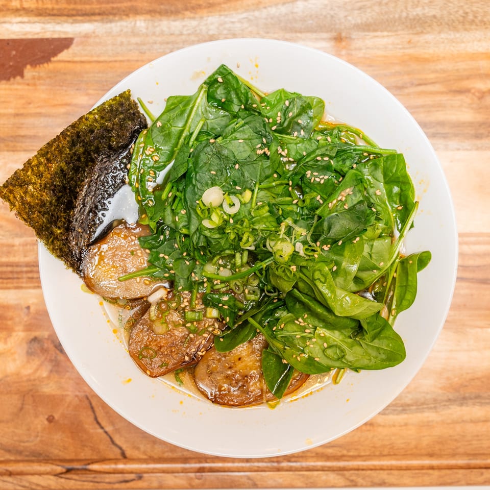 Bowl of saucy dumplings topped with fresh spinach, scallions, sesame seeds, and seaweed on a wooden table.