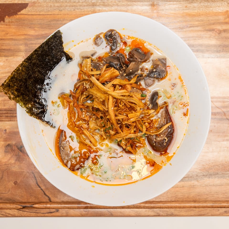 Top-down view of a spicy mushroom noodle soup topped with crispy shredded vegetables, sesame seeds, and seaweed.