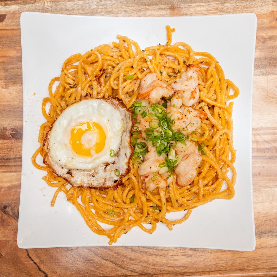 Creamy orange noodles topped with grilled shrimp, a fried egg, and sliced green onions on a white plate.