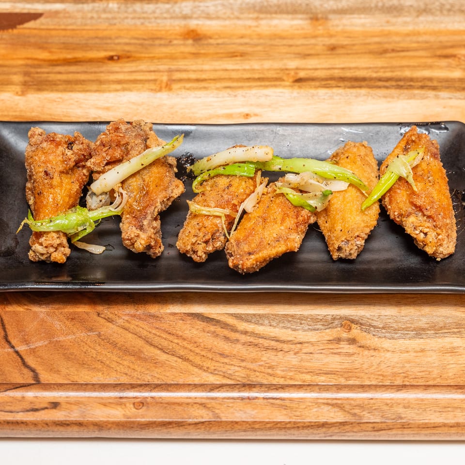 Crispy fried chicken pieces topped with sautéed green peppers and onions on a black rectangular platter.